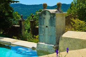 A stone structure with a pool, surrounded by greenery and hills in the background.