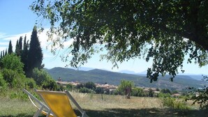 A yellow folding chair under a tree with a view of rolling hills and distant mountains.
