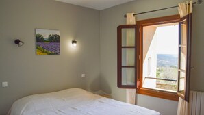 A bedroom with a bed, a painting, a window with curtains, and a view of the outdoors.