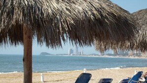 Una playa con sombrillas de paja y sillas de descanso azules frente al océano.