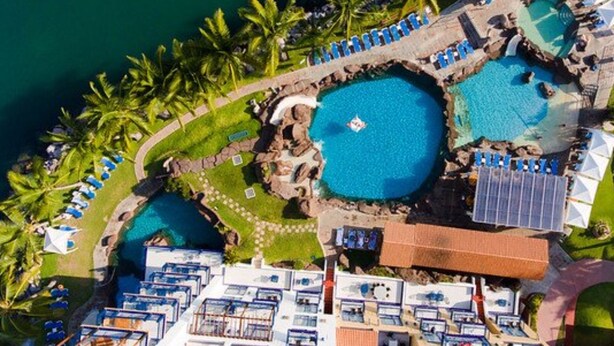 Vista aérea de un resort con múltiples piscinas, palmeras y diversas opciones de alojamiento, incluyendo bungalows sobre el agua y habitaciones estándar.
