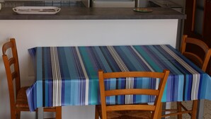 Uma cozinha compacta com armários de madeira, micro-ondas e geladeira. Há uma mesa de jantar com toalha de mesa listrada e duas cadeiras.