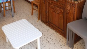 Quarto com um armário de madeira, televisão, mesa de jantar com cadeiras, um banco e duas fotos emolduradas na parede.