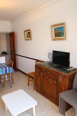 A room with a wooden cabinet, a television, a dining table with chairs, a bench, and two framed pictures on the wall.