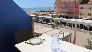 Varanda com mesa posta para dois, com vista para a praia e um edifício de hotel.
