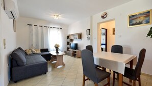 A modern living room with a grey sofa, a coffee table, and a dining area with a table and chairs. - Apartment in Vir with Terrace, Air condition, WIFI (4592-1) (Vir)