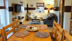 Uma sala de estar acolhedora com uma mesa de jantar de madeira, cadeiras, um sofá e uma televisão.