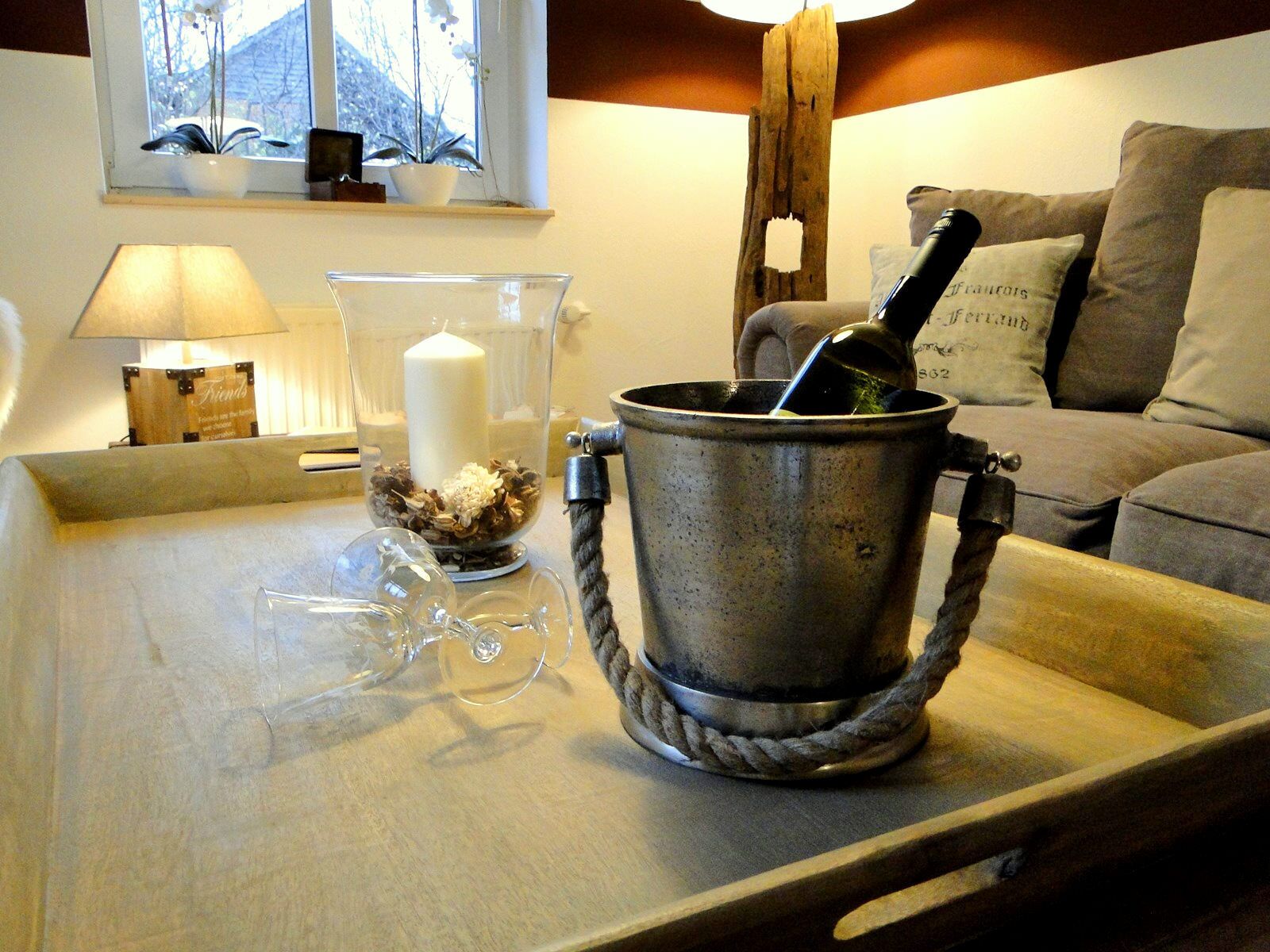 Una sala de estar acogedora con una mesa de centro de madera, una vela, un florero de vidrio y una botella de vino.