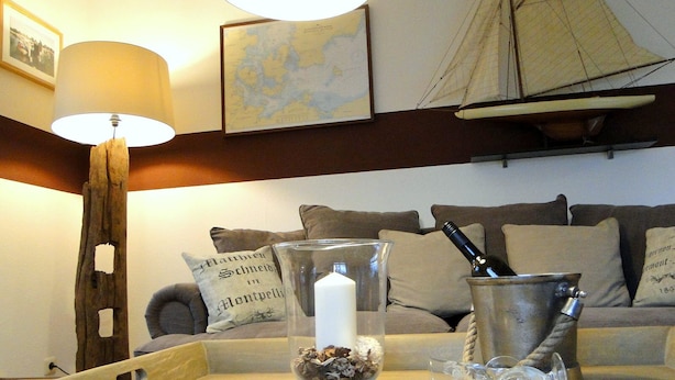 Uma sala de estar aconchegante com uma luminária, um modelo de navio, um mapa e um vaso de vidro com flores secas sobre um suporte.