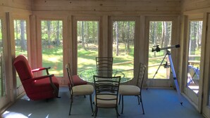 Una habitación con paneles de madera, una mesa y sillas de vidrio, un telescopio y una silla roja.