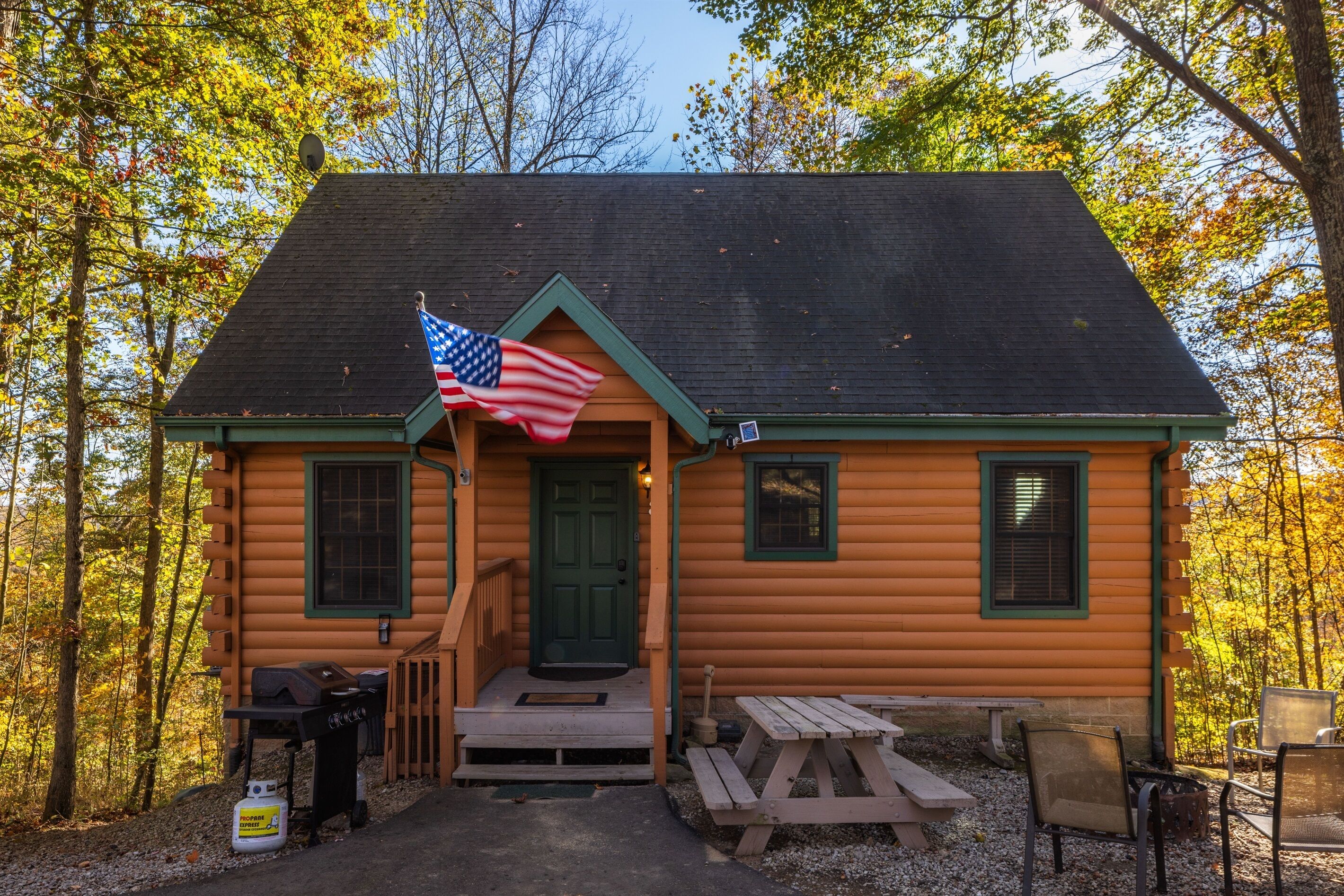 Eine Blockhütte mit Veranda, einer Flagge, einem Grill und Picknicktischen.