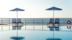 A swimming pool with two blue-striped lounge chairs and umbrellas, a lifebuoy, and a view of the sea. - Seafront luxury apartment with amazing sunset view 3 (Stavros,Chania)
