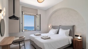 A bedroom with a bed, bedside table, chair, and a view of the sea through an open window. - Seafront luxury apartment with amazing sunset view 3 (Stavros,Chania)