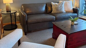 A modern living room with a leather sofa, two armchairs, a coffee table, and a large deer painting on the wall.