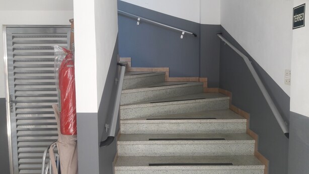 A staircase with a handrail, a red plastic bag, and a metal grate on the left. - Furnished apartment near the beach (Canto do Forte)