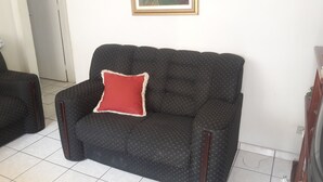 A black sofa with a red cushion and a small table beside it. - Furnished apartment near the beach (Canto do Forte)