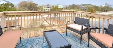 A deck with wicker furniture, a patterned rug, and a view of houses in the background.