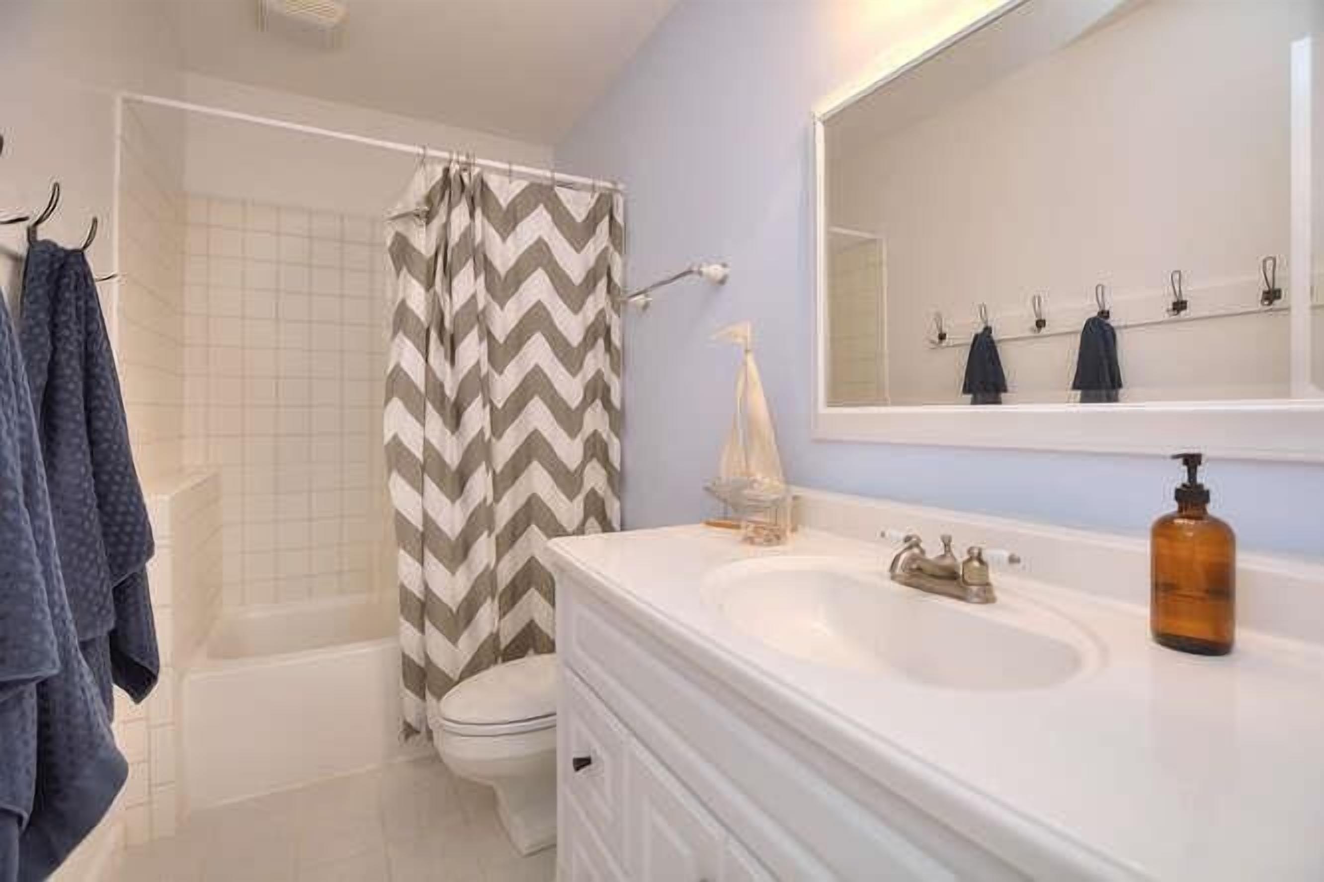 Un baño con lavamanos blanco, un espejo, cortina de ducha y un inodoro.