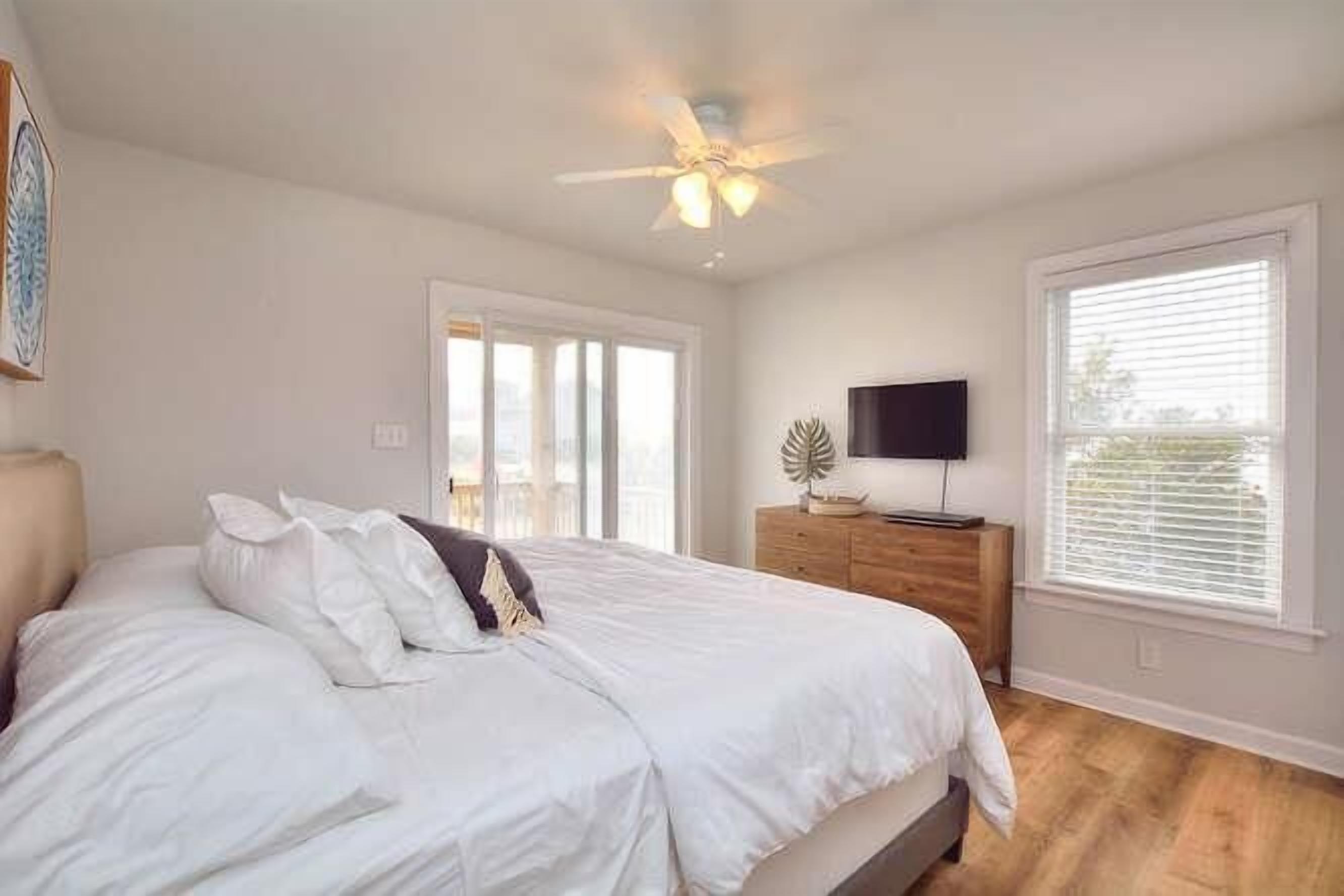 Un dormitorio con cama, ventilador de techo, televisor, cómoda y ventana.