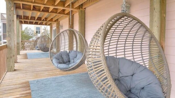 Une terrasse en bois avec des fauteuils en osier suspendus, dotés de coussins.