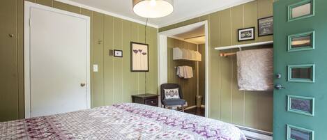 A bedroom with a bed, a chair, a door, and a hanging light fixture.
