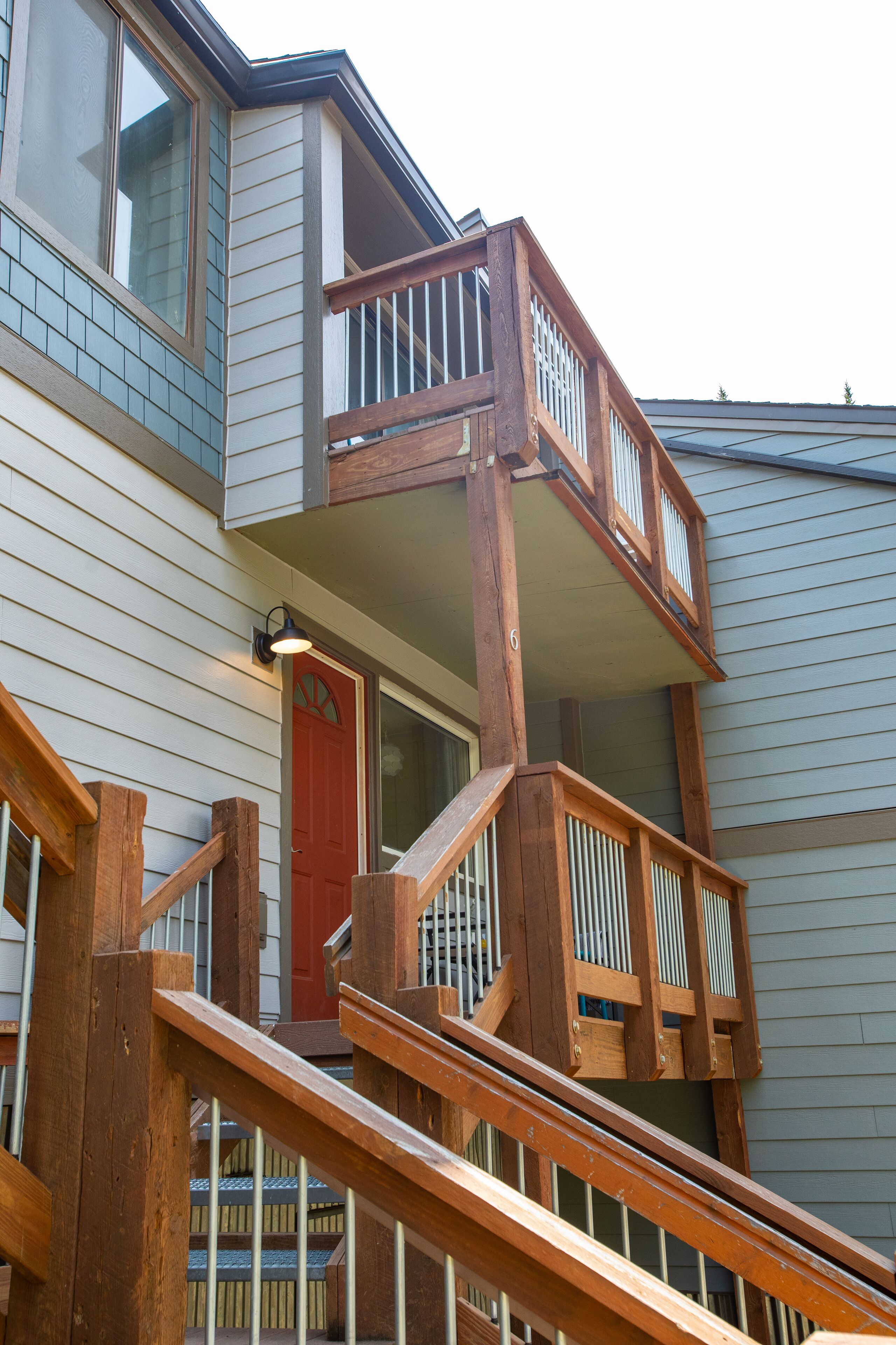 Eine mehrstöckige Holztreppe führt zu einer roten Tür, mit einem Balkon auf der oberen Ebene.