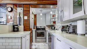 Una cucina moderna con mobili bianchi, forno integrato, macchina del caffè e tostapane.