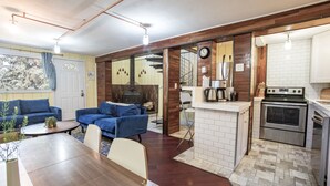 Una cucina moderna con piano cottura, forno e schienale piastrellato bianco. C'è un'area pranzo con tavolo in legno e divani blu. Una scala conduce a un piano superiore.
