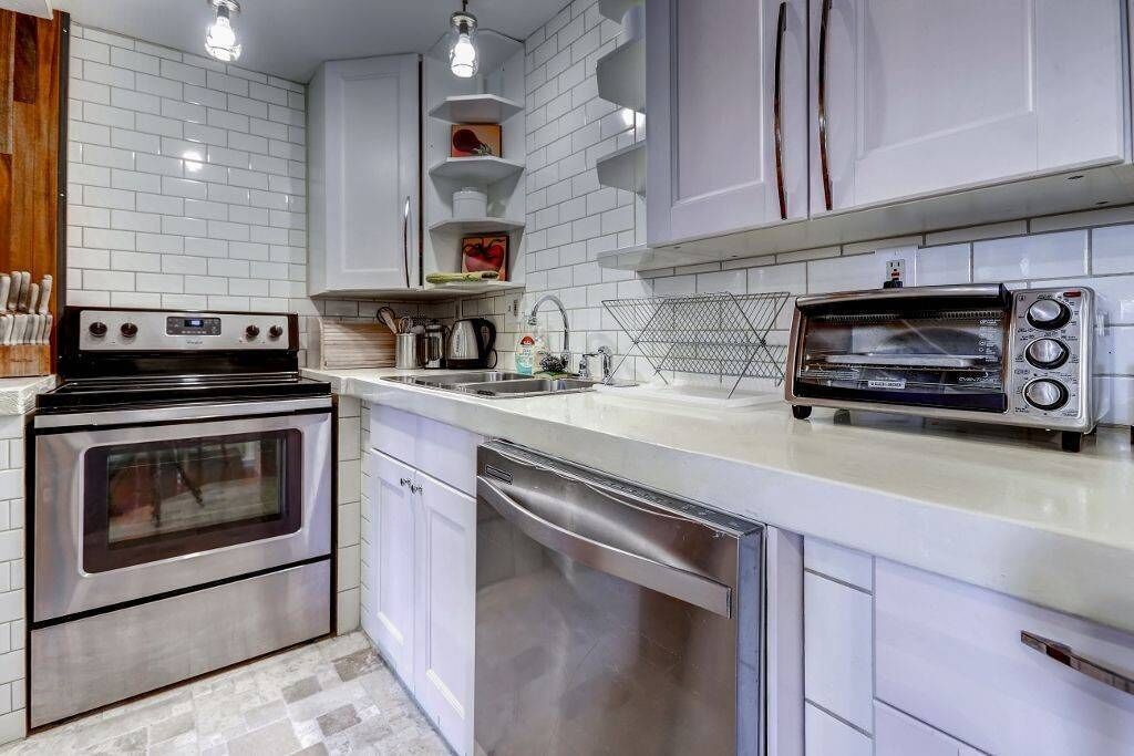 Una cocina moderna con armarios blancos, un horno de acero inoxidable, lavavajillas y horno tostador empotrado.