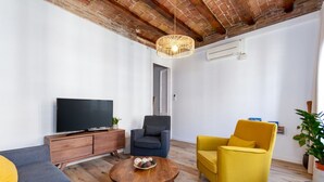 Ein Wohnzimmer mit Fernseher, Sofa, Sessel, Couchtisch und einer Pendelleuchte.
