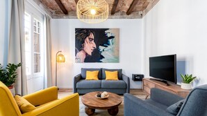 Ein Wohnzimmer mit einer Couch, Sesseln, einem Couchtisch, einem Fernseher und einem Gemälde an der Wand.