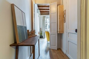 A narrow hallway with a wooden table, a potted plant, and a yellow chair.
