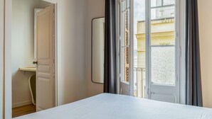 Ein Hotelzimmer mit einem Bett, einer Tür zu einem Badezimmer und einem Fenster mit Blick auf Gebäude.