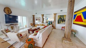 A spacious living room with a large white sofa, a flat-screen TV, and a dining area with a table and chairs.