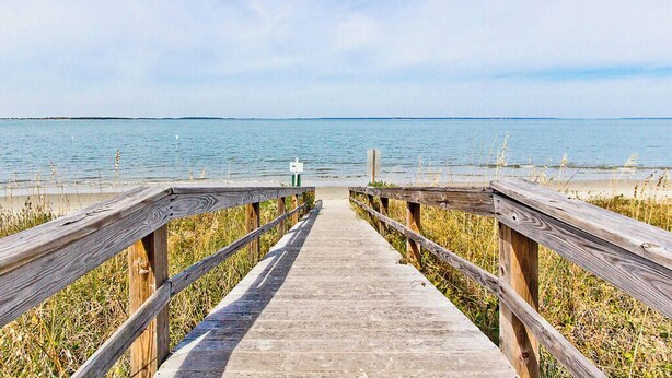 A wooden boardwalk leading to a beach with a clear view of the water and sky.
