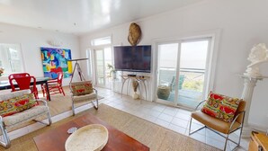 A spacious living room with a large TV, red chairs, and a colorful abstract painting.