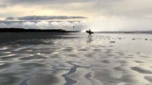 Una spiaggia con una persona che trasporta una tavola da surf.