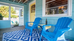 Un portico con poltrone Adirondack blu, un tavolo e un tappeto decorato.