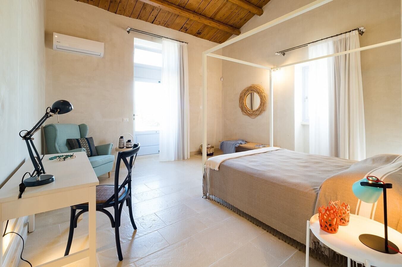 Quarto com cama, escrivaninha, cadeira e uma mesinha de cabeceira com abajur.