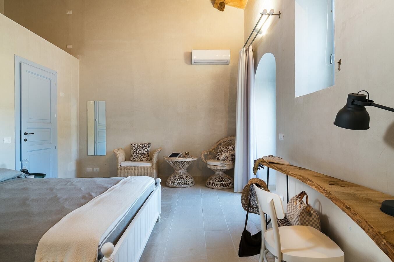 Ein Schlafzimmer mit Bett, Nachttisch, Sessel, rundem Tisch und Spiegel.