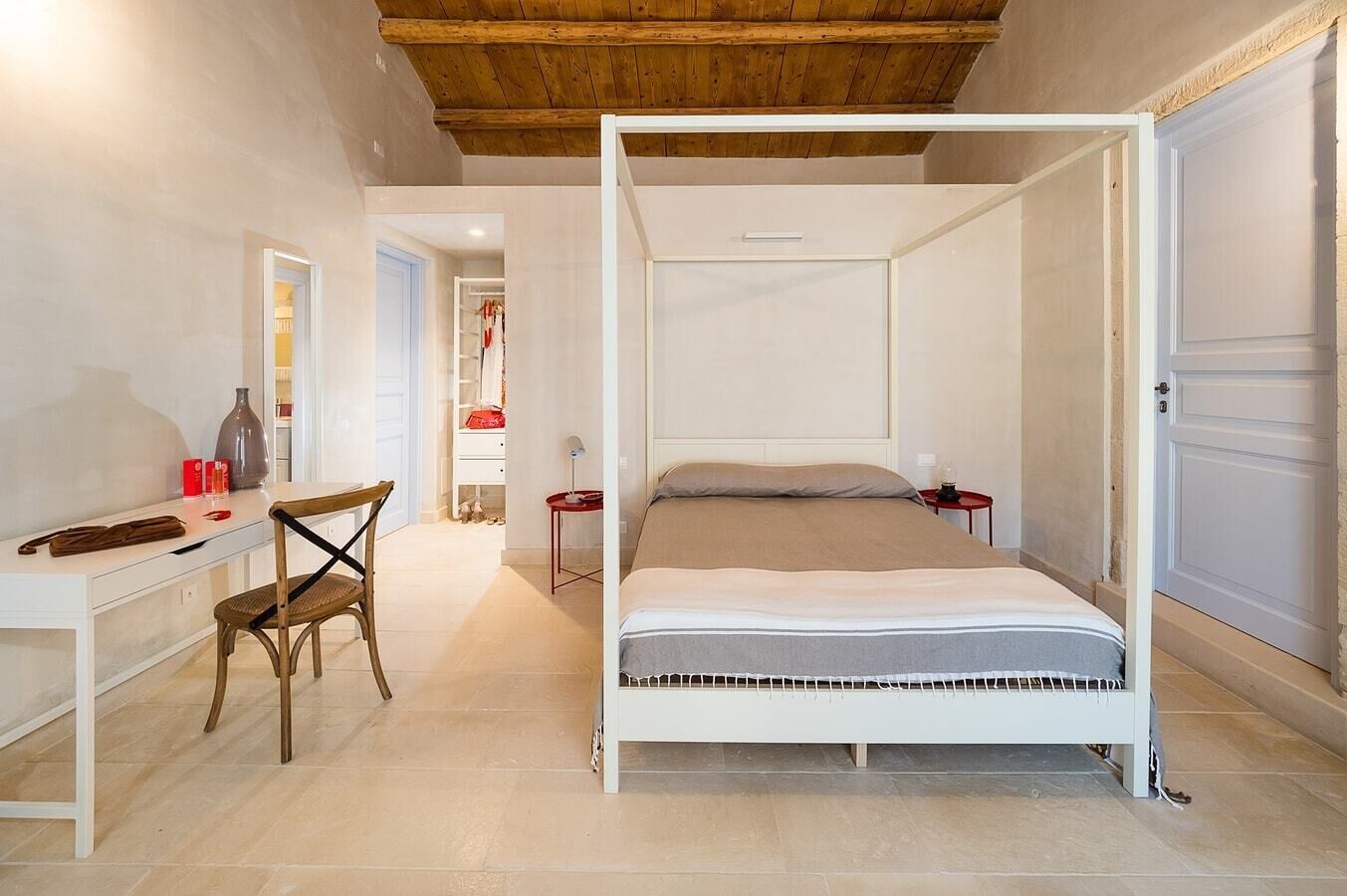 A bedroom with a four-poster bed, a desk with a chair, and a wardrobe.
