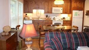 A compact kitchen with wooden cabinets, a microwave, and a dining area with a table and chairs. - 'Ski Shack' Condo w/ Private Deck (Sugar Mountain)