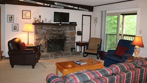 A cozy living room with a stone fireplace, a television, and comfortable seating. - 'Ski Shack' Condo w/ Private Deck (Sugar Mountain)