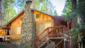 Una cabaña rústica con chimenea de piedra, fachada de madera y una escalera que lleva a una terraza.