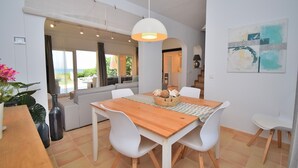 Un espace repas avec une table en bois, des chaises blanches et un luminaire suspendu.