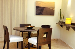 Un coin repas avec une table ronde, quatre chaises, une bougie et un tableau représentant un coucher de soleil sur la plage accroché au mur.