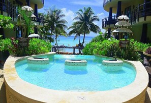 Ein Poolbereich mit Blick auf das Meer, umgeben von Palmen und Liegestühlen.