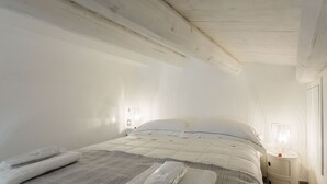 A neatly made bed with a striped blanket, a bedside table with a lamp, and a window with sheer curtains. - Suite behind the cathedral (Palermo)