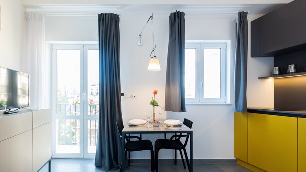 A modern kitchen with a dining area, featuring a table set for two, a TV, and a view through the window. - Suite behind the cathedral (Palermo)