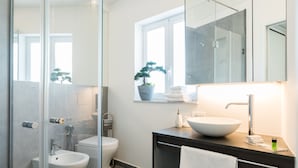 A modern bathroom with a glass shower enclosure, a bidet, a toilet, a sink with a large mirror, and a potted plant. - Suite behind the cathedral (Palermo)